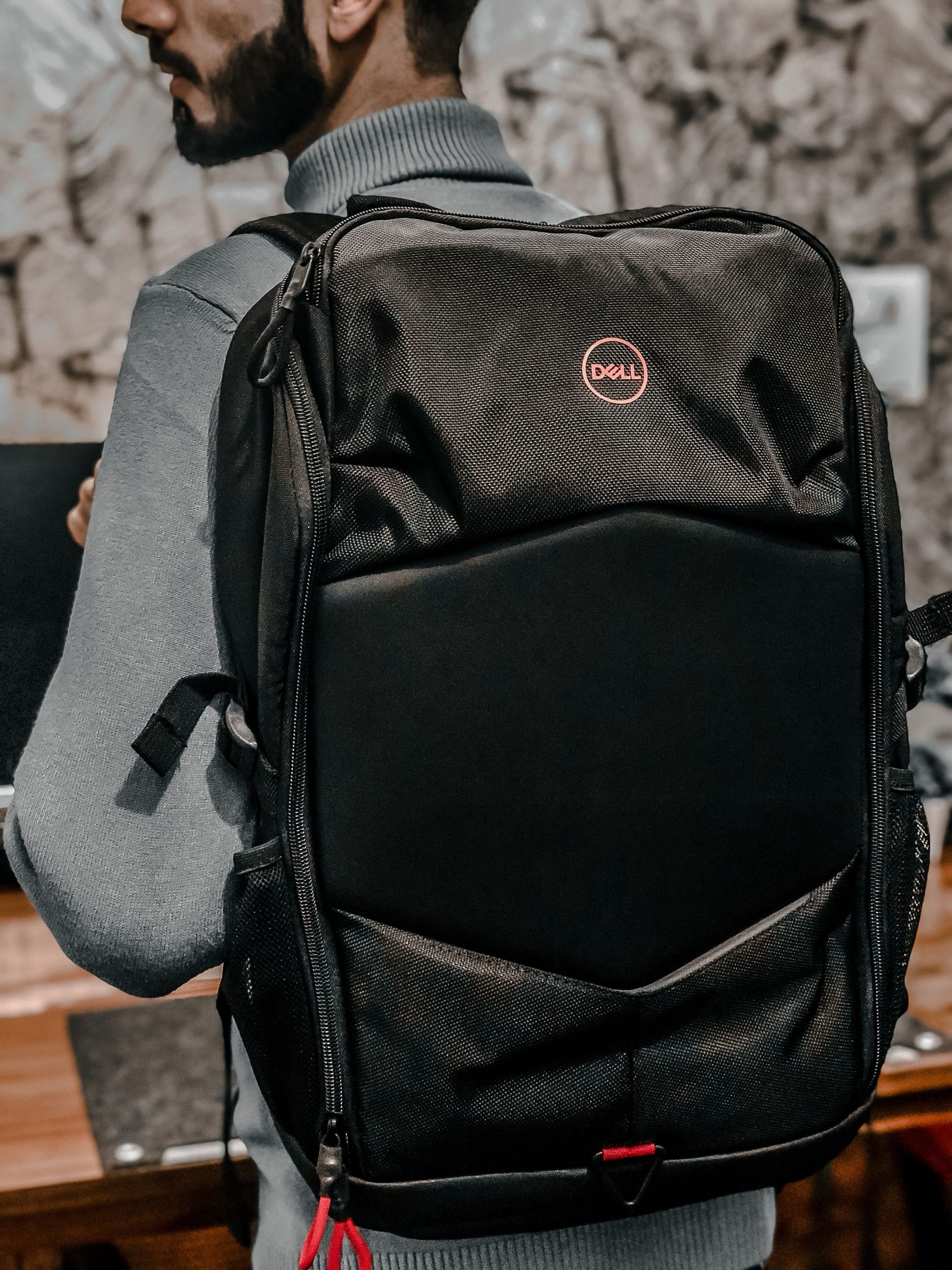 Close-up of a man wearing a Dell backpack indoors with a blurred background.